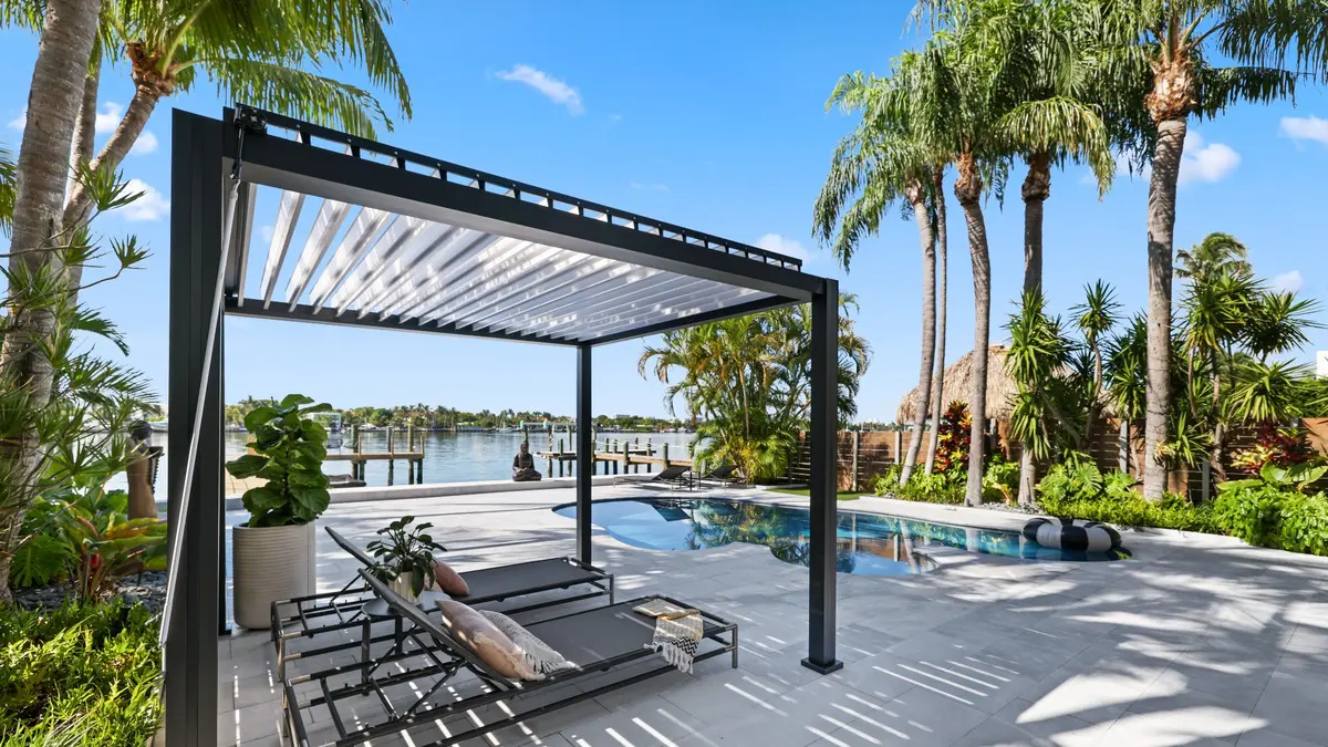 Black K-BANA pergola with white louvers and lounge chairs beside a waterfront pool